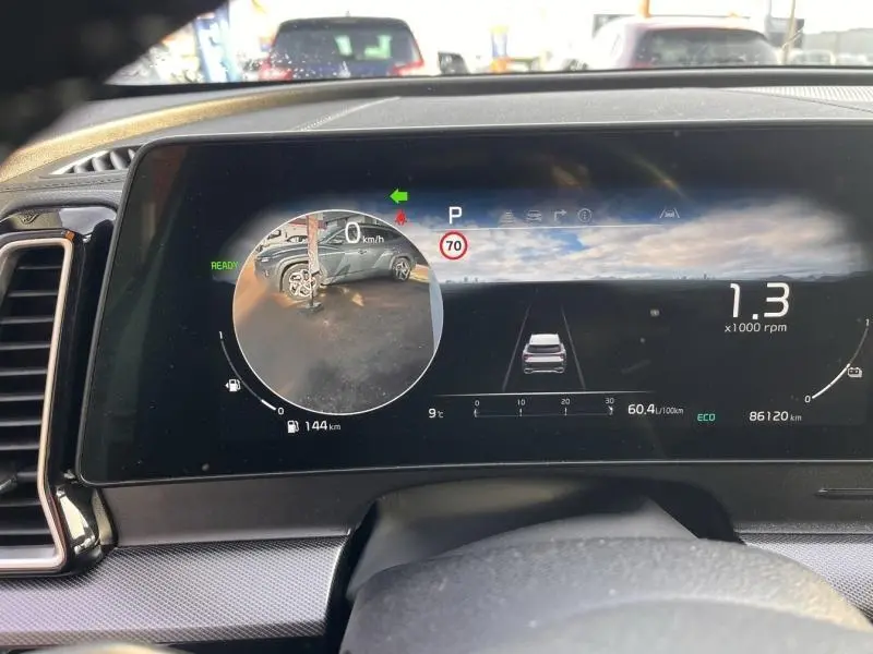 Affichage numérique du tableau de bord du Kia Sportage blanc, montrant la caméra de recul et les indicateurs de vitesse et régime moteur.