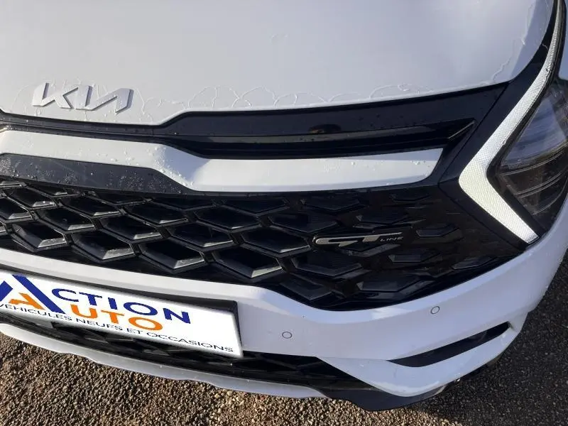 Gros plan sur la calandre avant noire et le logo GT-Line du Kia Sportage blanc nacré 2022, avec phares LED en forme de boomerang.