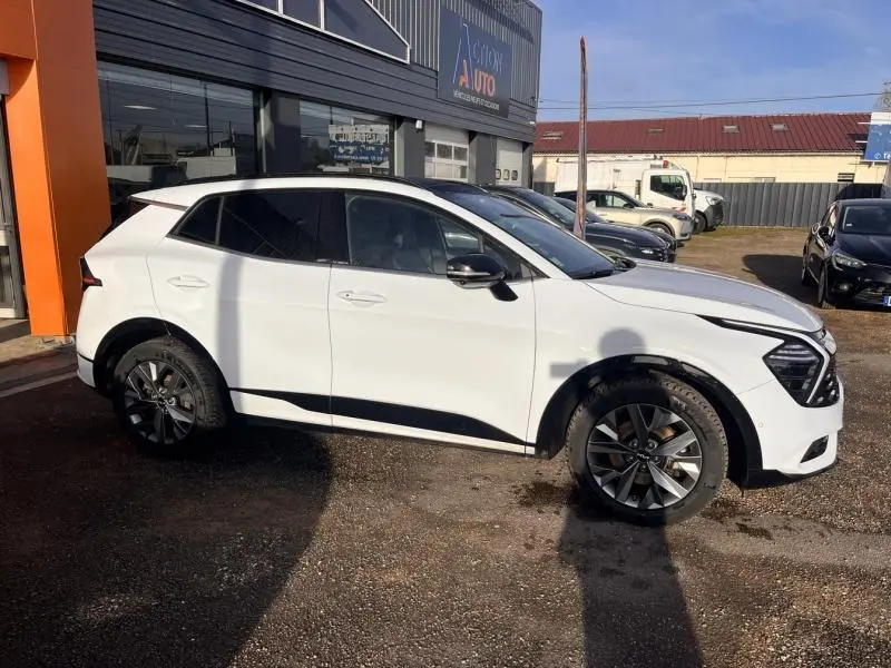 Vue de profil droit du Kia Sportage blanc nacré avec jantes alliage et vitres arrière surteintées, stationné devant un garage.