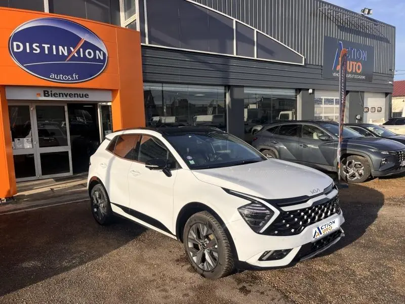KIA SPORTAGE blanc nacré en vue 3/4 avant droit, avec calandre noire et jantes alliage devant un garage.
