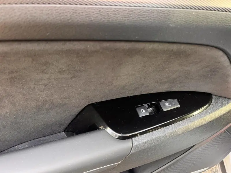 Détail de la commande de verrouillage des portes sur la garniture intérieure noire et suédée du côté gauche du KIA Sportage blanc nacré.
