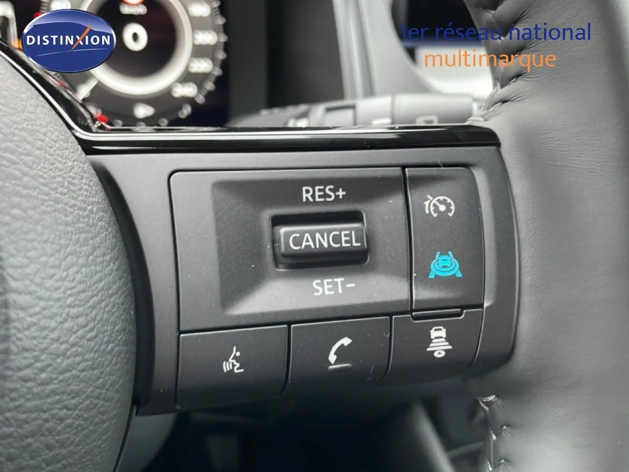 Gros plan sur les commandes au volant gris du Nissan Qashqai blanc nacré, avec boutons de régulateur et assistance conduite.