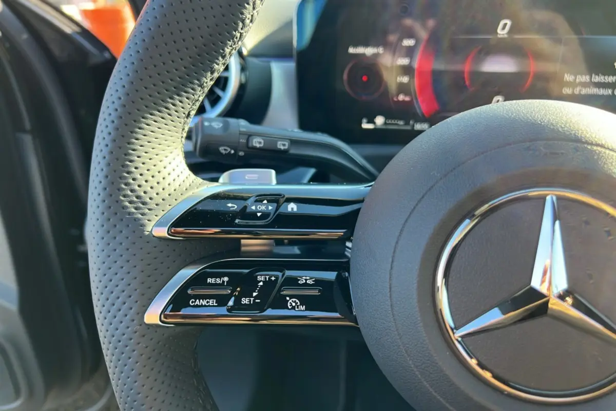 Gros plan sur le volant cuir perforé noir de la Mercedes Classe A 200D BVA Exclusive Design avec commandes multifonctions et logo étoile central.