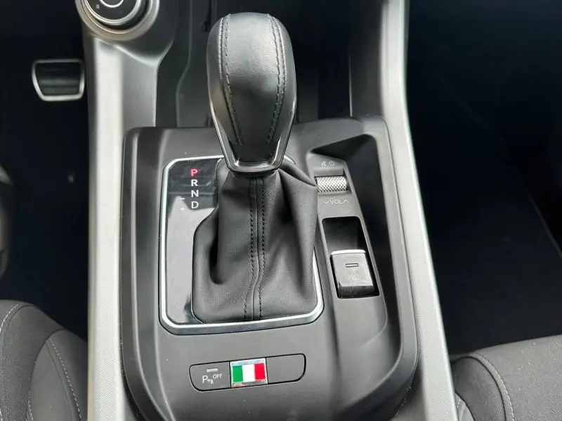 Gros plan sur le levier de vitesse automatique noir de l'Alfa Romeo Tonale 1.5 Hybrid, avec drapeau italien et commandes autour.