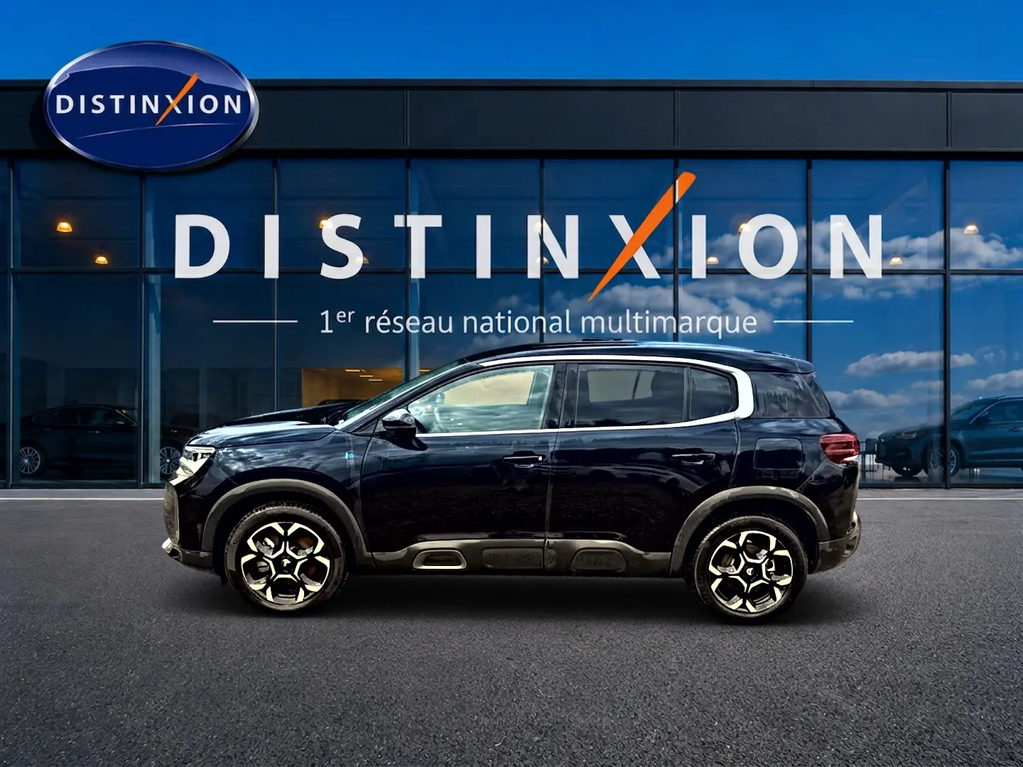 Profil latéral droit du Citroën C5 Aircross noir 2024 avec jantes alu et barres de toit visibles devant une vitrine Distinxion.