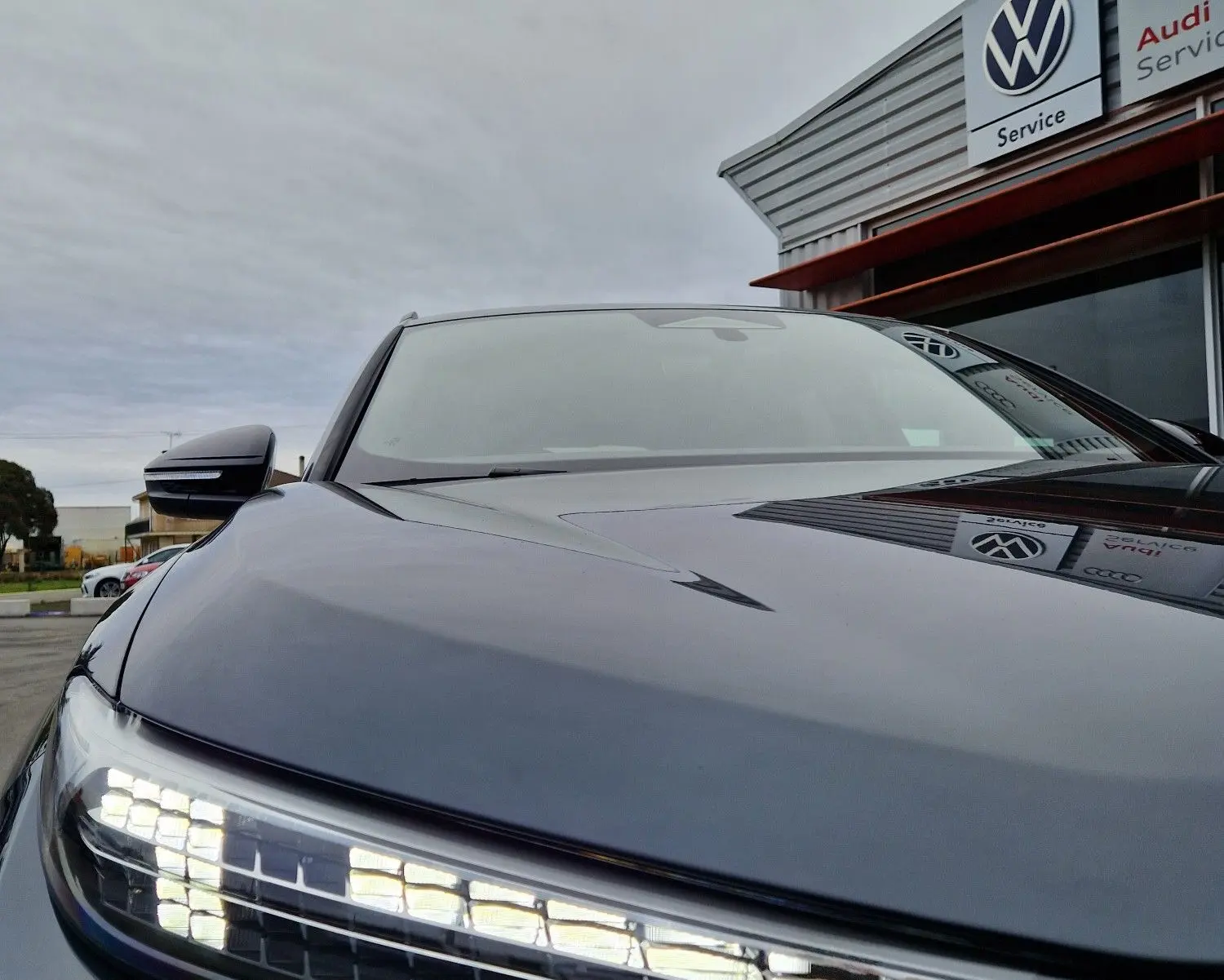 Gros plan sur le phare avant gauche allumé d'un Audi Q6 e-tron Performance S-Line gris Manhattan, vue en légère contre-plongée.