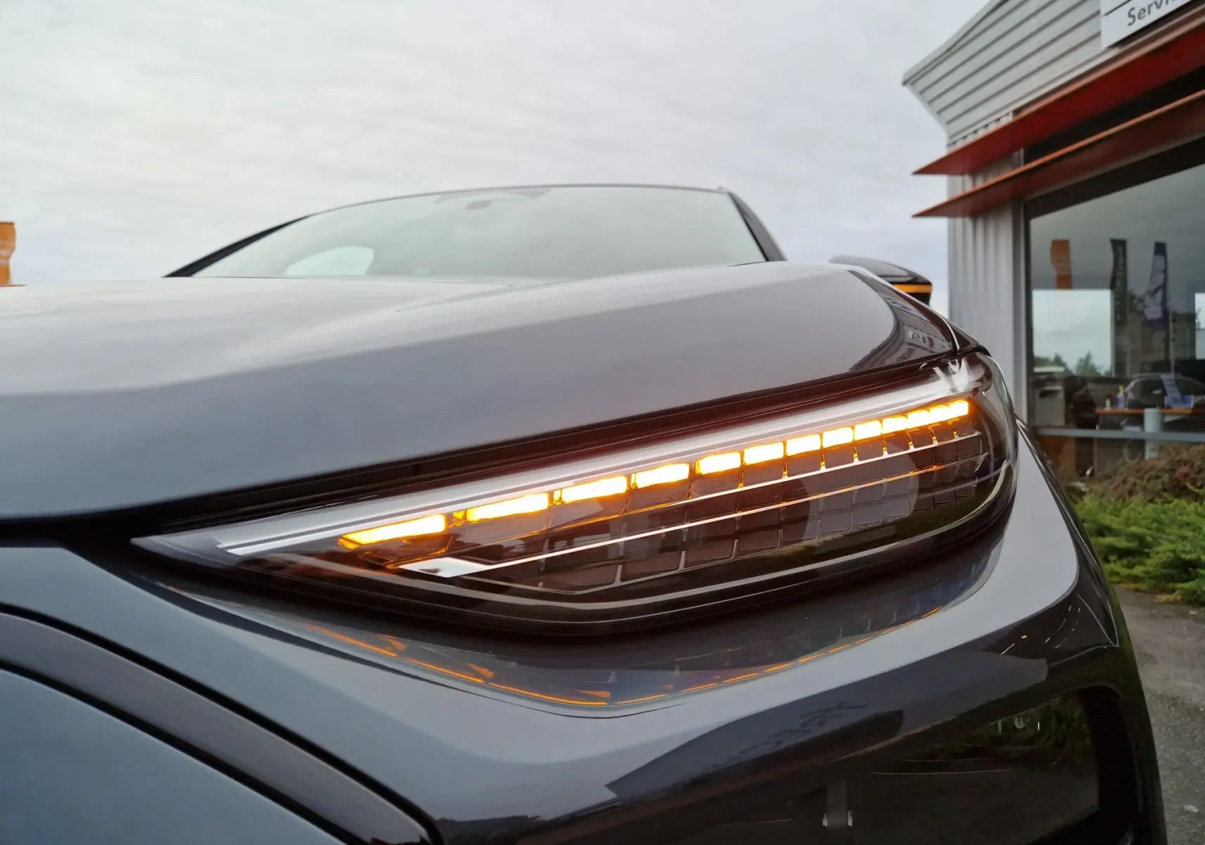 Gros plan sur le feu avant droit allumé d'un Audi Q6 e-tron Performance S-Line gris Manhattan, 2025.