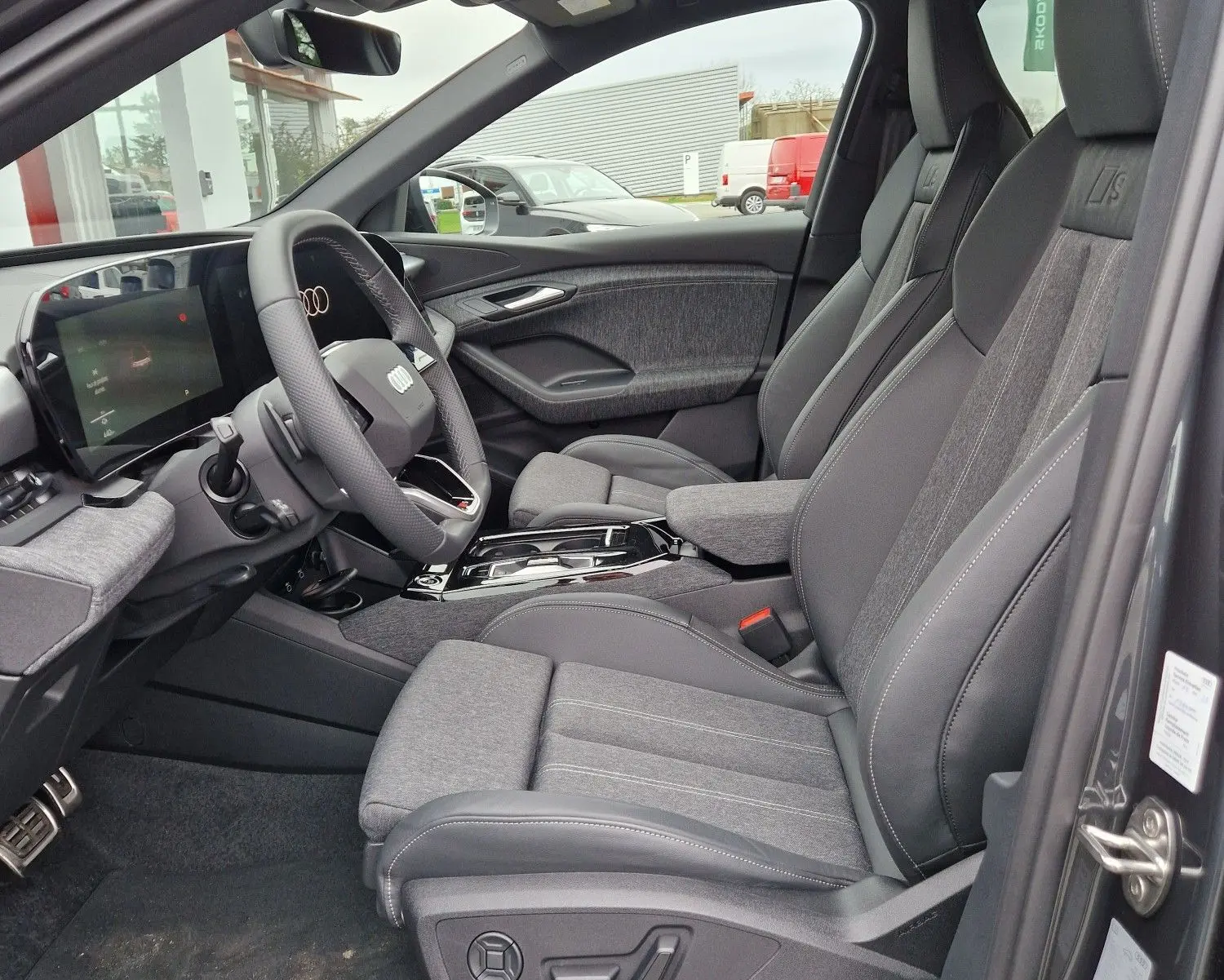 Intérieur côté conducteur de l'Audi Q6 e-tron Performance S-Line gris Manhattan, sièges sport avec logo S et tableau de bord numérique.