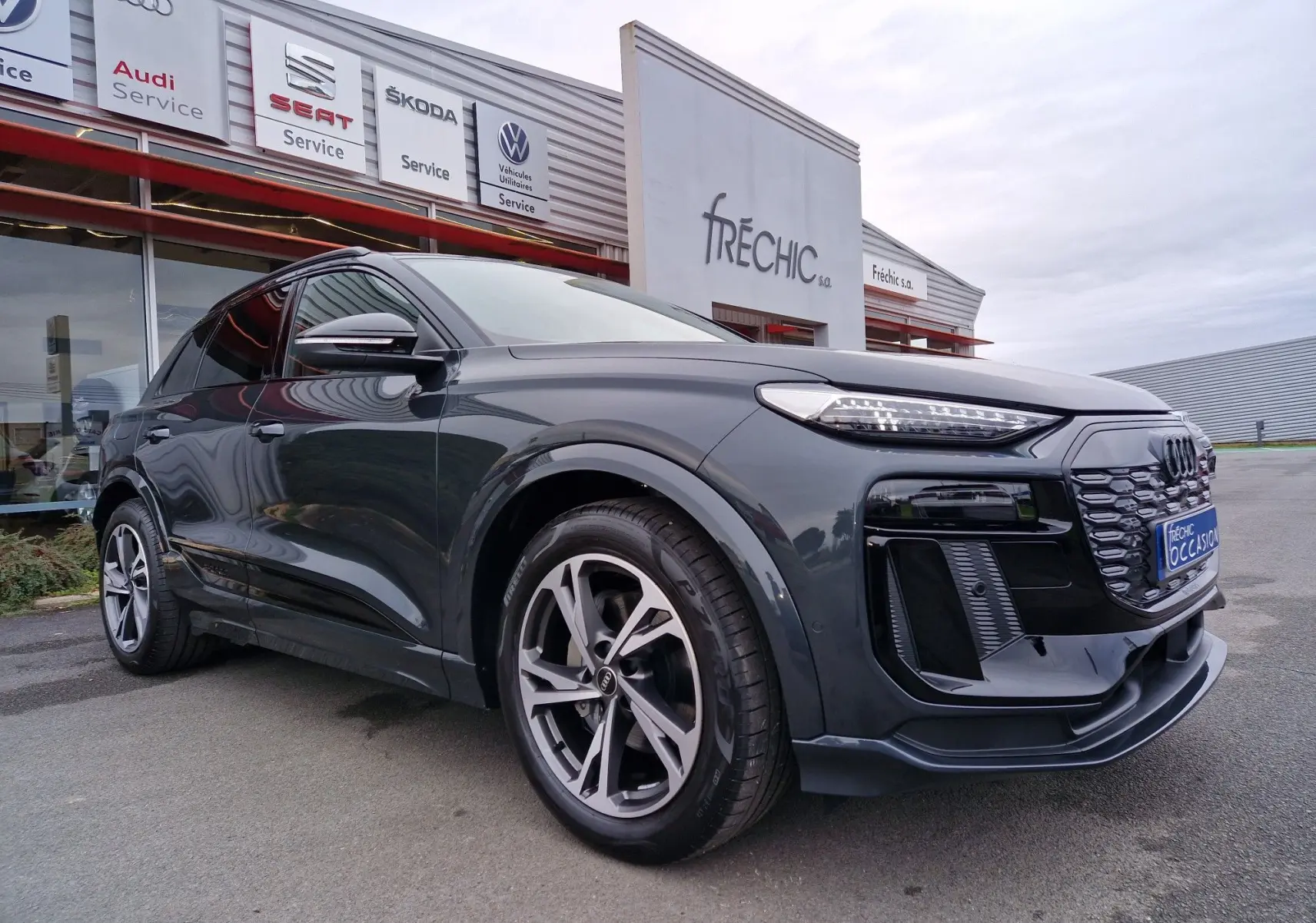 Audi Q6 e-tron Performance S-Line gris Manhattan en 3/4 avant droit, avec jantes Audi Sport et pack esthétique noir.