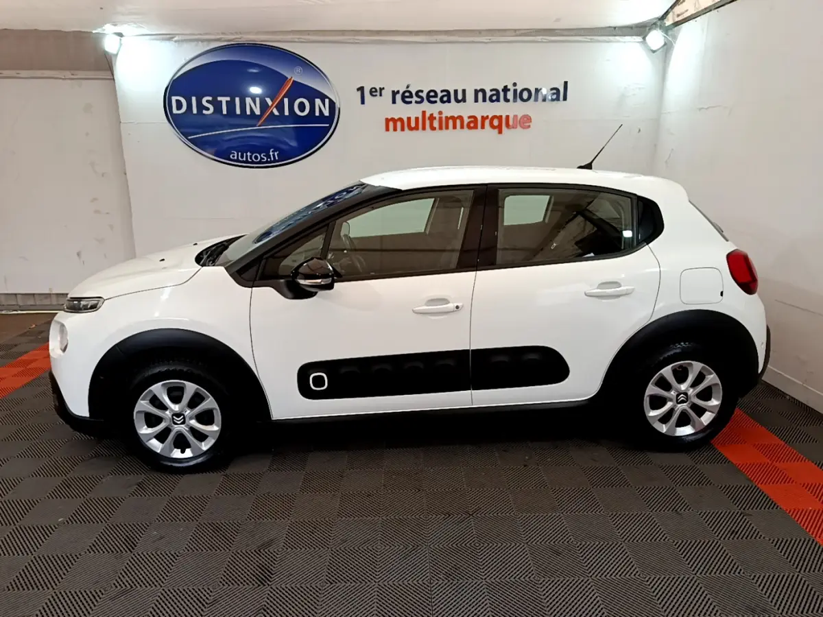 Profil droit d'une Citroën C3 blanche de 2019 avec protections noires sur les portières, en intérieur showroom.