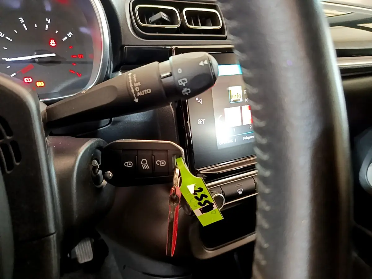 Vue rapprochée du tableau de bord et volant cuir noir d'une Citroën C3 blanche, avec clé insérée et écran tactile allumé.