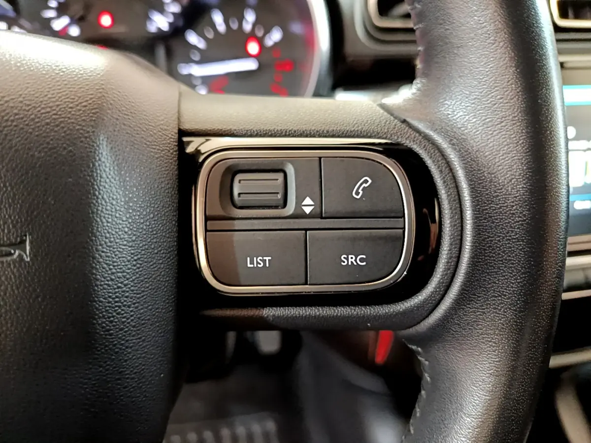Gros plan sur les commandes gauche du volant cuir de la Citroën C3 blanche, avec boutons de gestion audio et appels.
