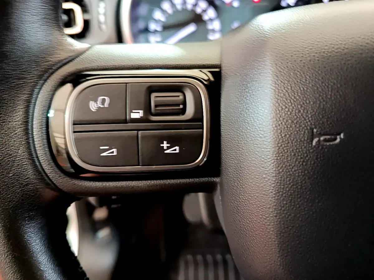 Gros plan sur les commandes gauche du volant cuir de la Citroën C3 blanche, modèle 2019, avec boutons multifonctions.