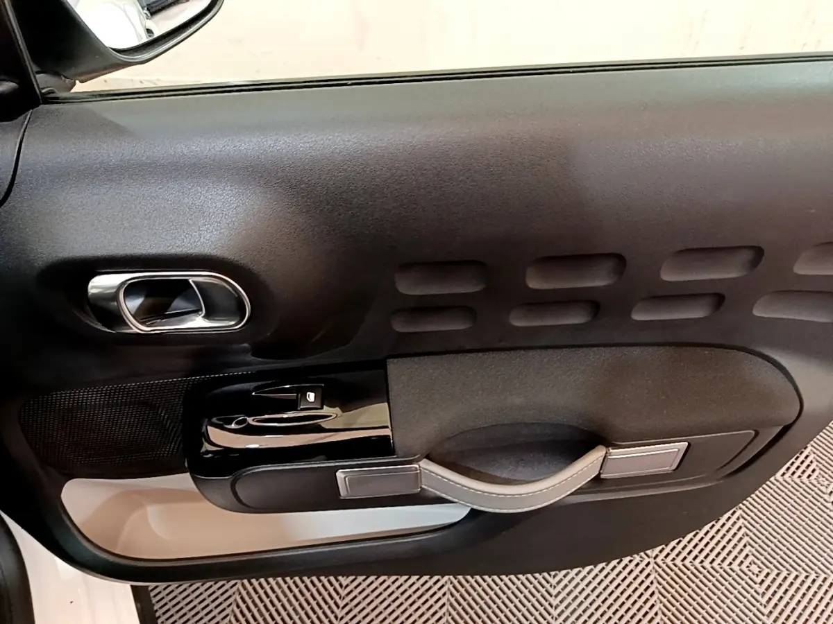 Vue rapprochée de la porte intérieure côté conducteur d'une Citroën C3 blanche, avec poignée et commandes noires.