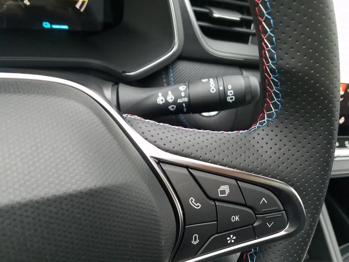 Détail du volant perforé avec surpiqûres tricolores et commandes intégrées dans un Renault Captur gris Rafale 2025.