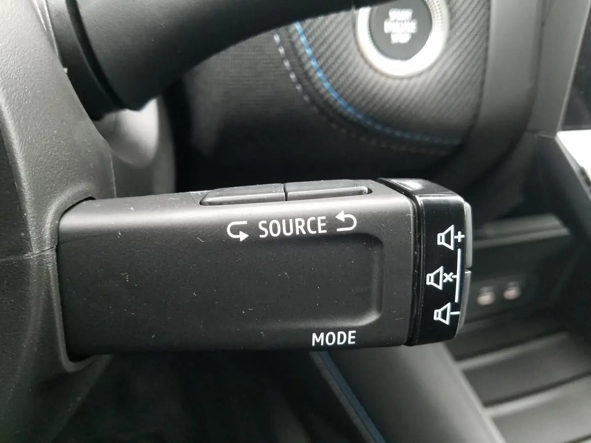Gros plan sur la commande au volant du Renault Captur 2025, avec boutons source et mode visibles sur fond noir.