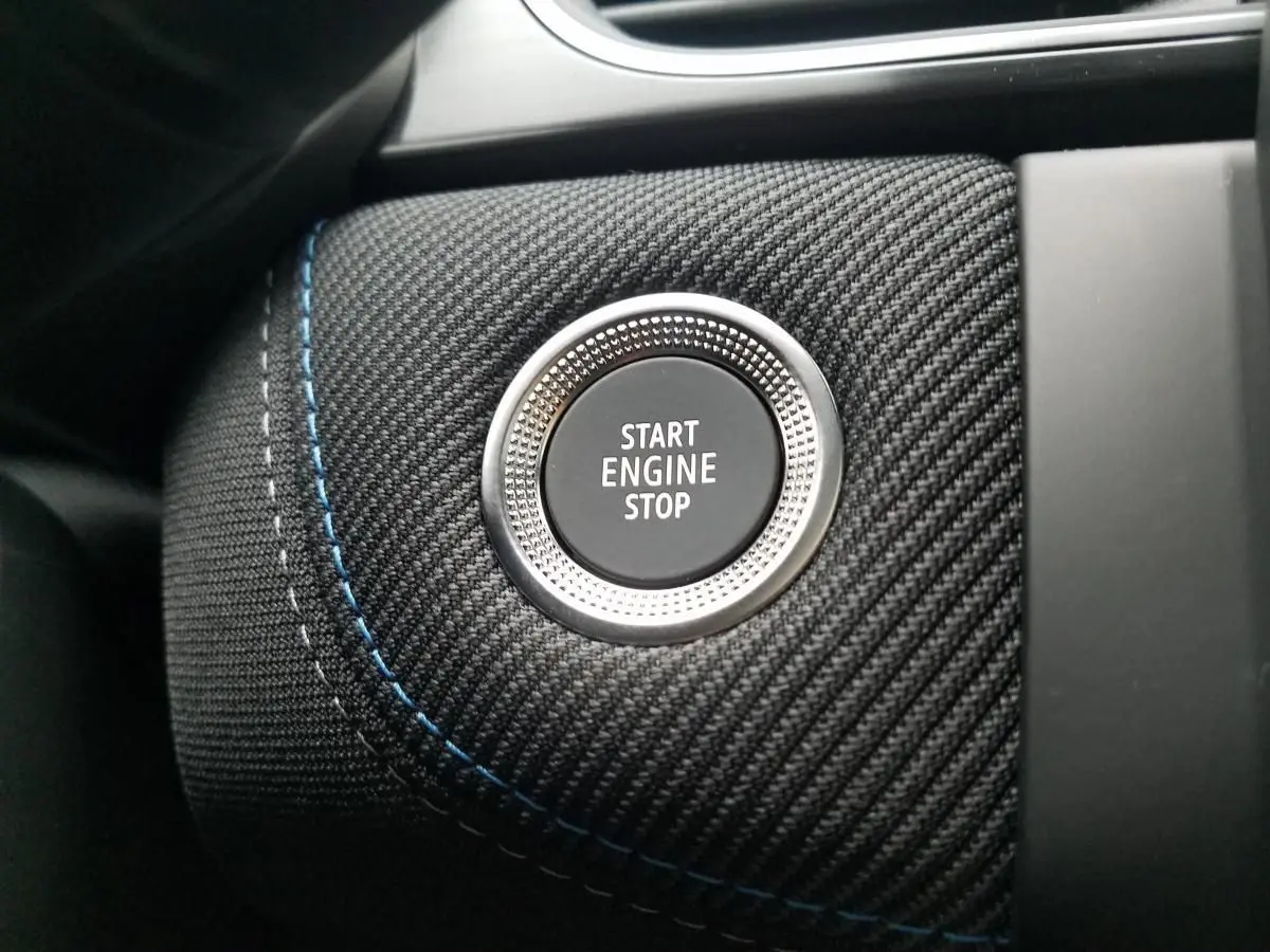 Gros plan sur le bouton Start Engine Stop entouré de tissu noir texturé avec surpiqûres bleues dans un Renault Captur 2025.