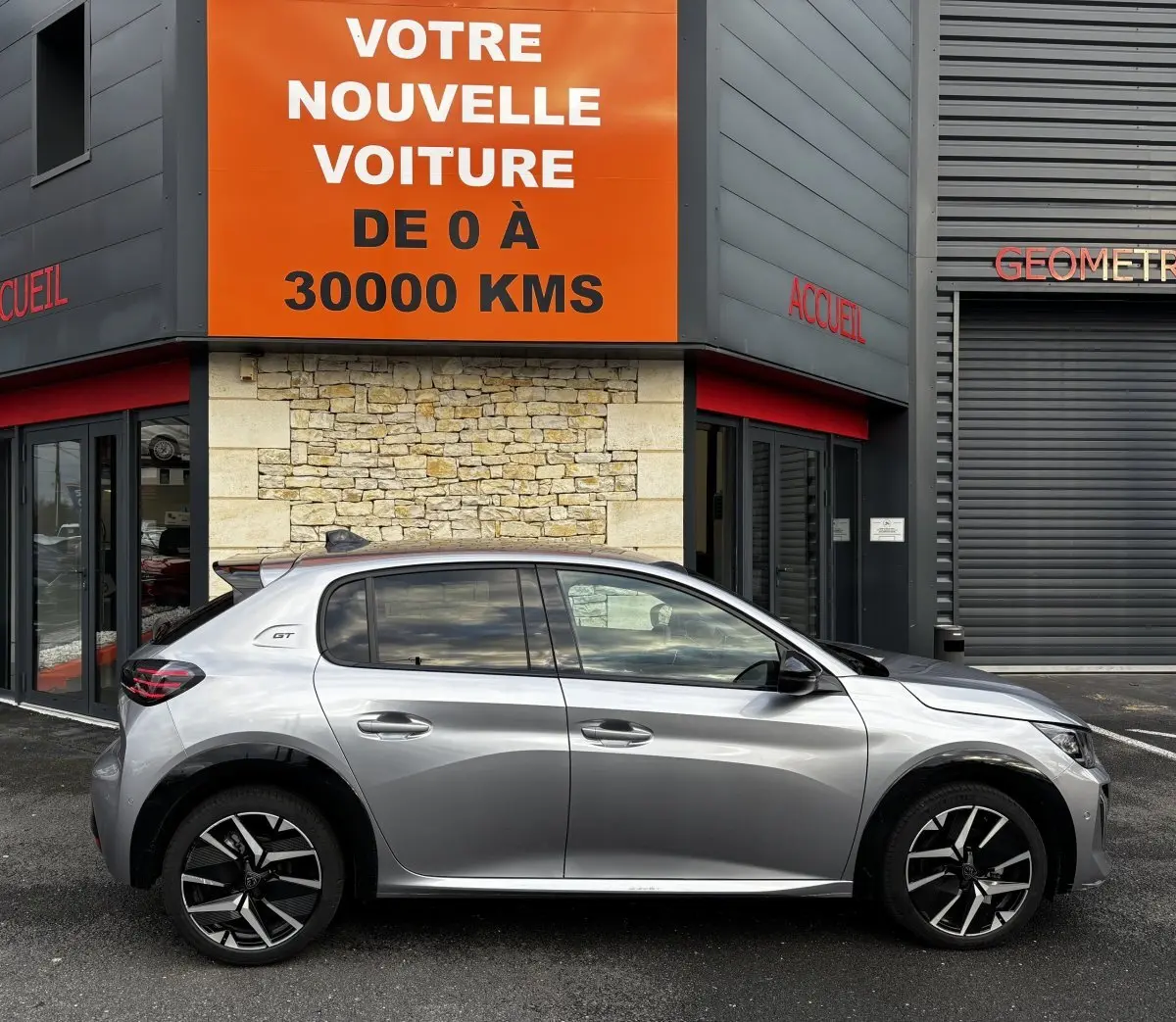 Profil côté gauche d'une Peugeot 208 Hybrid 110 e-DCS6 GT gris clair, avec jantes noires et détails GT visibles.