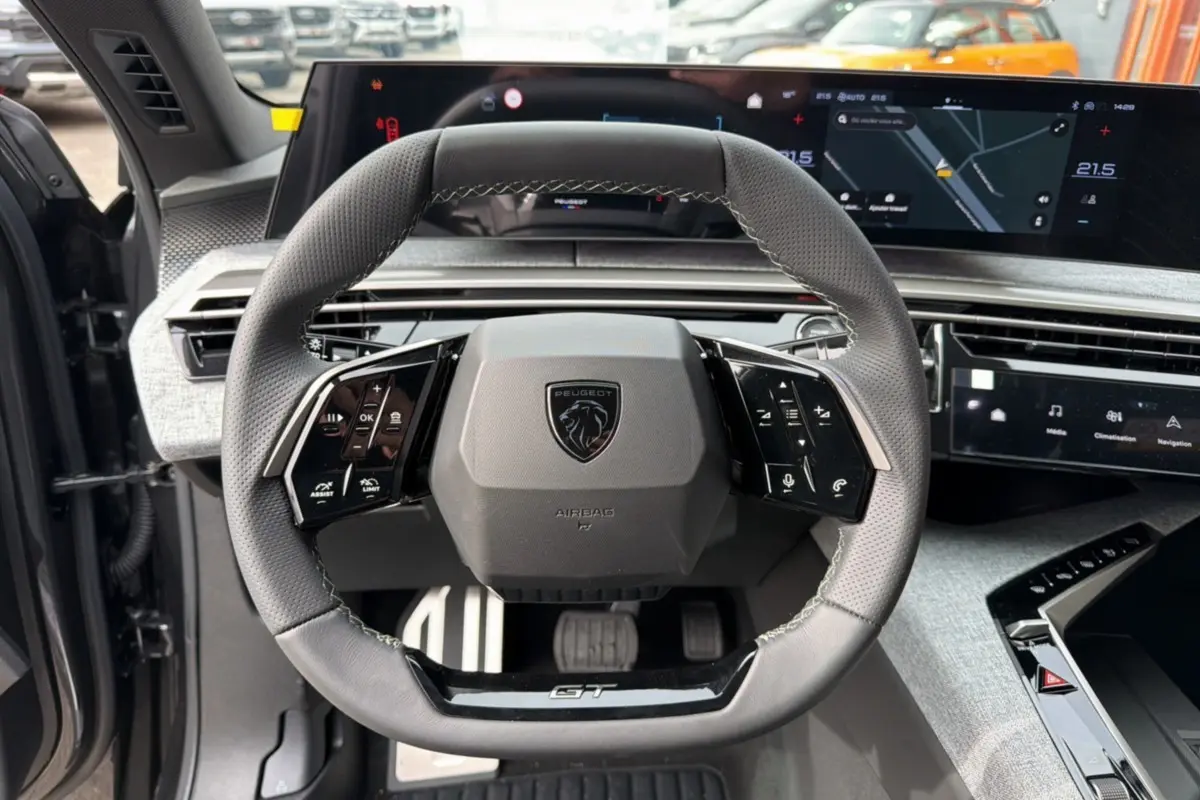 Vue rapprochée du volant cuir multifonctions Peugeot 3008 Hybrid GT 2025 avec tableau de bord numérique et pédalier aluminium.