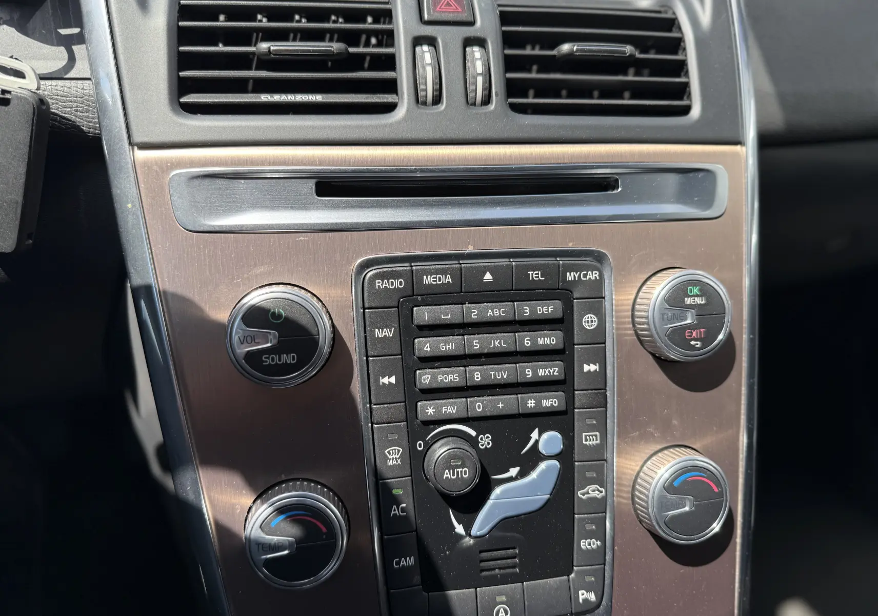 Vue rapprochée de la console centrale du Volvo XC60 gris foncé, montrant les commandes audio et climatisation.