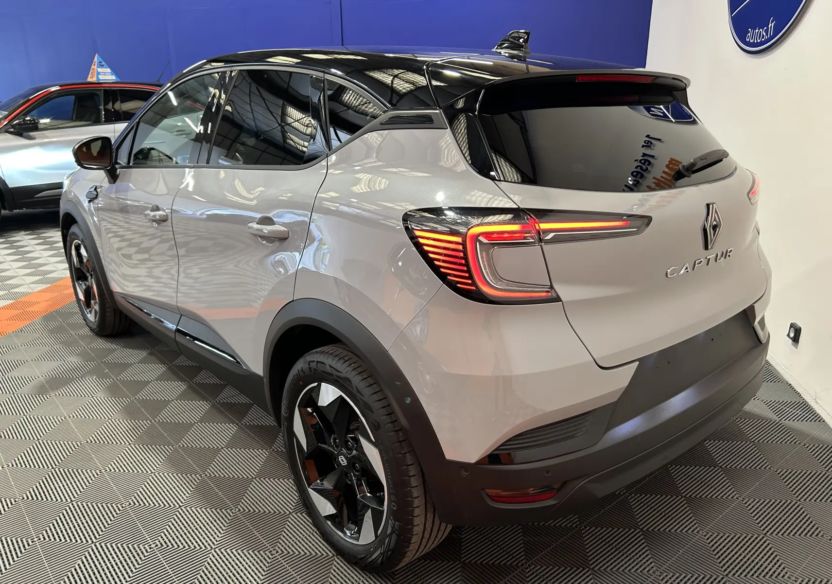 Vue 3/4 arrière droite du Renault Captur gris Rafale avec toit noir et feux arrière LED allumés en intérieur showroom.