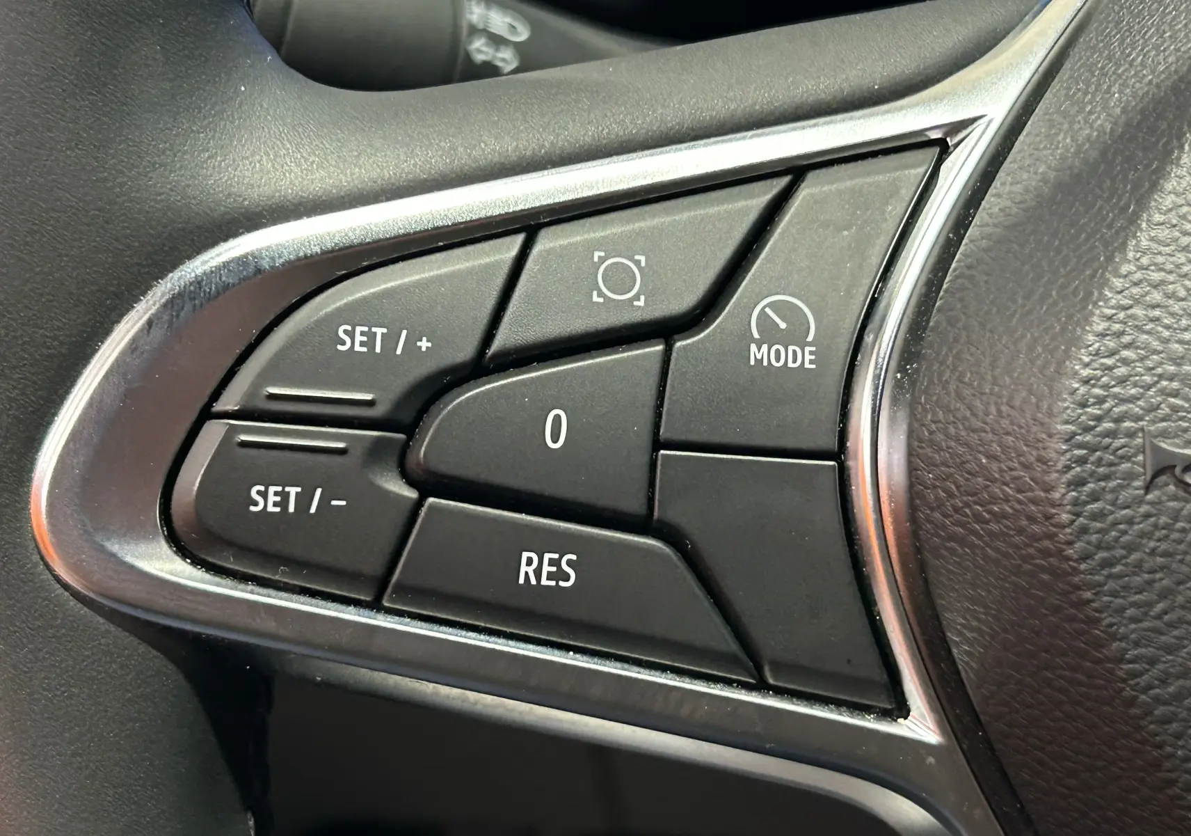 Gros plan sur les commandes noires du volant côté gauche du Renault Captur gris Rafale, boutons de régulateur de vitesse.