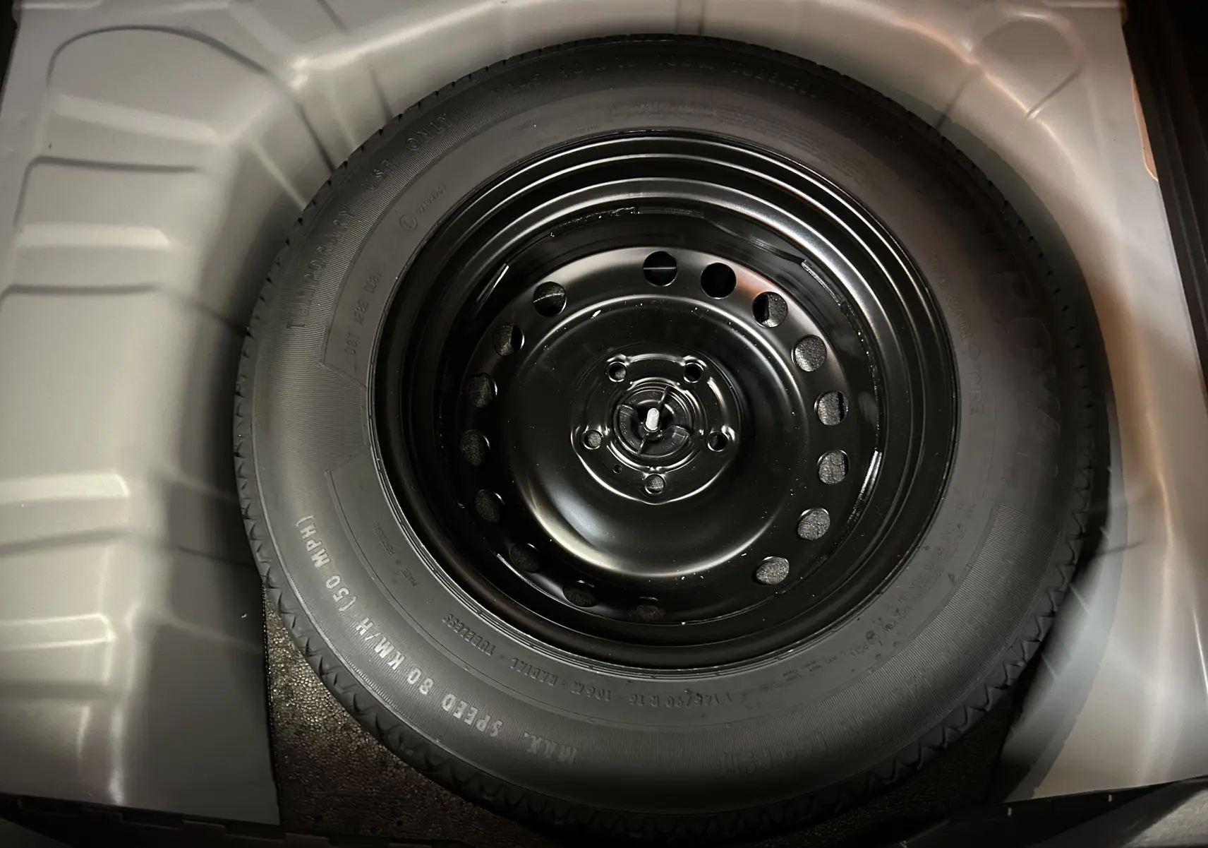 Gros plan sur la roue de secours noire dans le coffre du Renault Captur gris Rafale, vue de dessus.