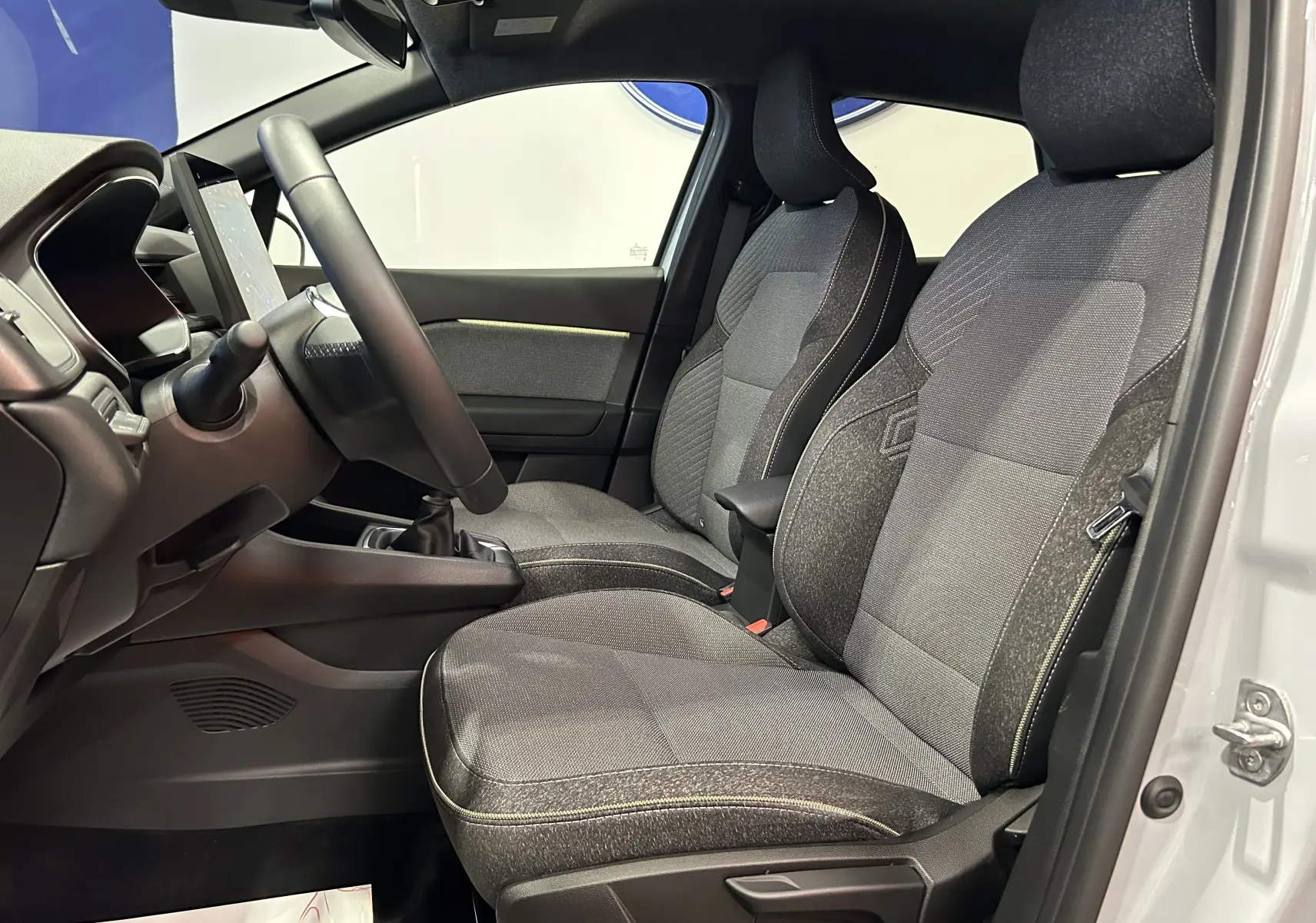 Vue intérieure côté conducteur du Renault Captur gris Rafale, montrant les sièges en tissu et le volant avec boîte manuelle.