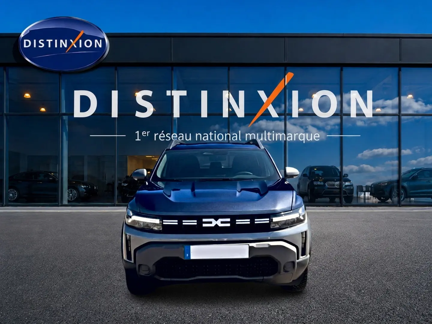 Vue avant d'un Dacia Duster gris schiste avec calandre lumineuse et logo distinctif, devant une vitrine Distinxion.