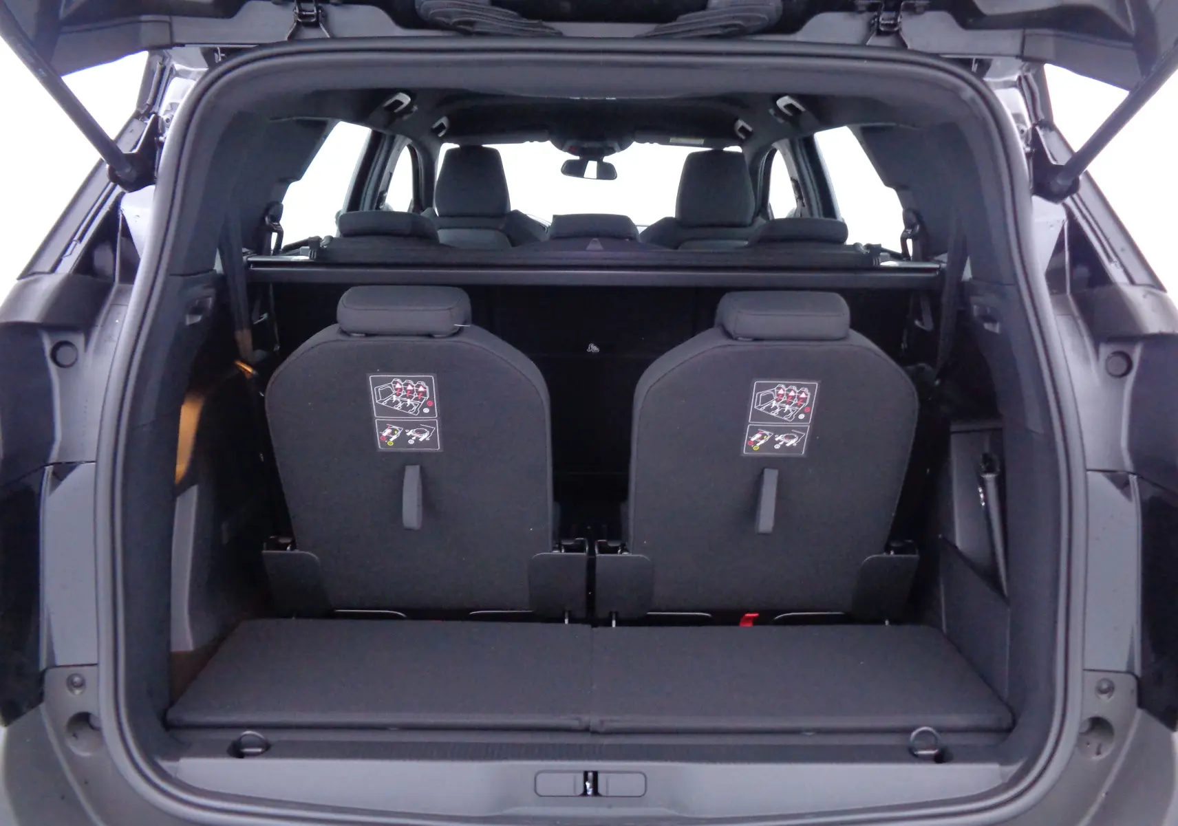 Vue arrière du coffre ouvert du Peugeot 5008 noir perle métal, montrant les sièges arrière rabattus et l'intérieur spacieux.