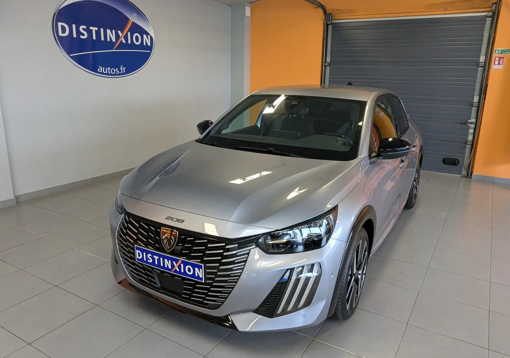 Vue 3/4 avant droite d'une Peugeot 208 Hybrid 145ch GT gris Artens en showroom avec logo Distinxion visible.