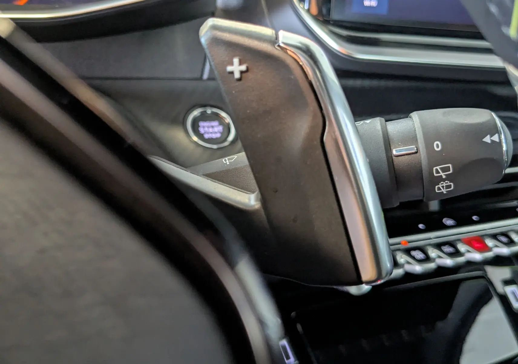 Gros plan sur la palette de changement de vitesse droite et bouton start/stop dans l’habitacle noir du Peugeot 208 Hybrid 145CH GT.
