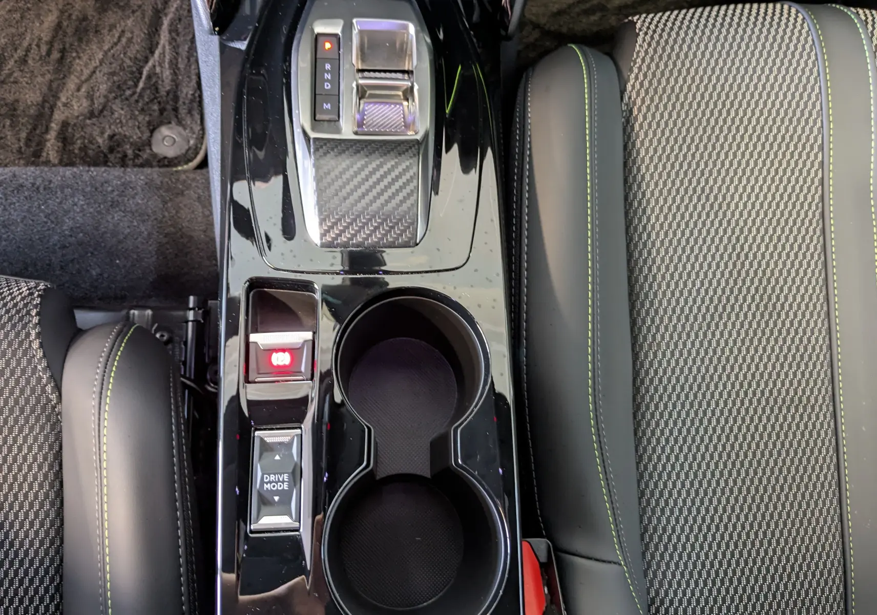 Vue plongeante sur la console centrale noire brillante de la Peugeot 208 Hybrid 145ch GT avec sièges gris à surpiqûres vertes.