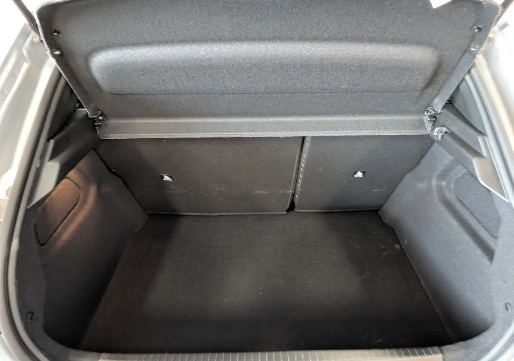 Coffre ouvert de la Peugeot 208 Hybrid 145ch GT gris Artens, vue intérieure montrant l'espace de chargement vide.
