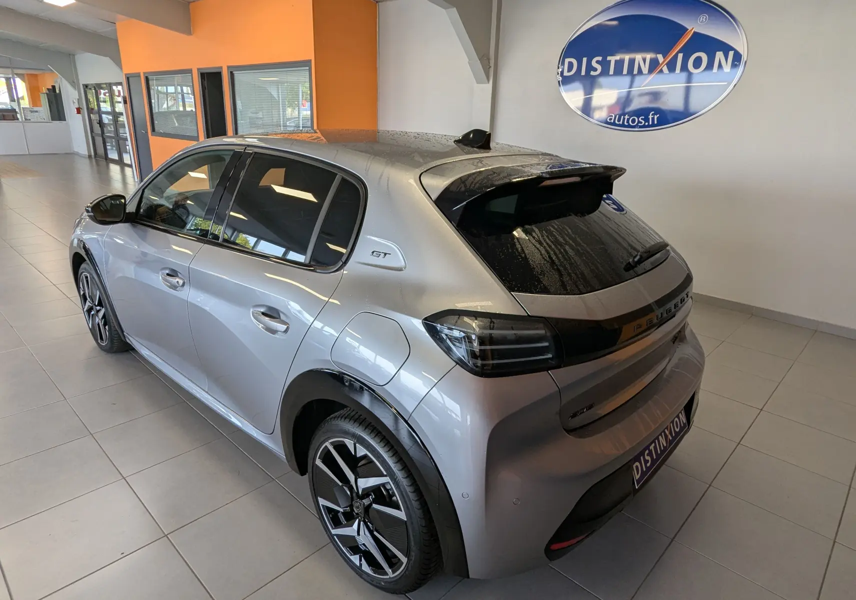 Vue 3/4 arrière droite d'une Peugeot 208 HYBRID 145CH GT gris Artens en showroom avec jantes bi-ton et vitres teintées.