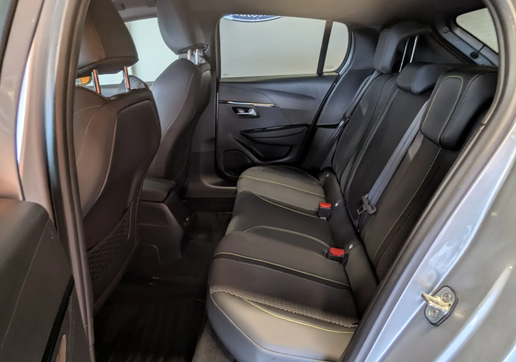 Vue intérieure côté droit sur la banquette arrière noire avec surpiqûres vertes d'une Peugeot 208 Hybrid 145ch GT gris Artens.
