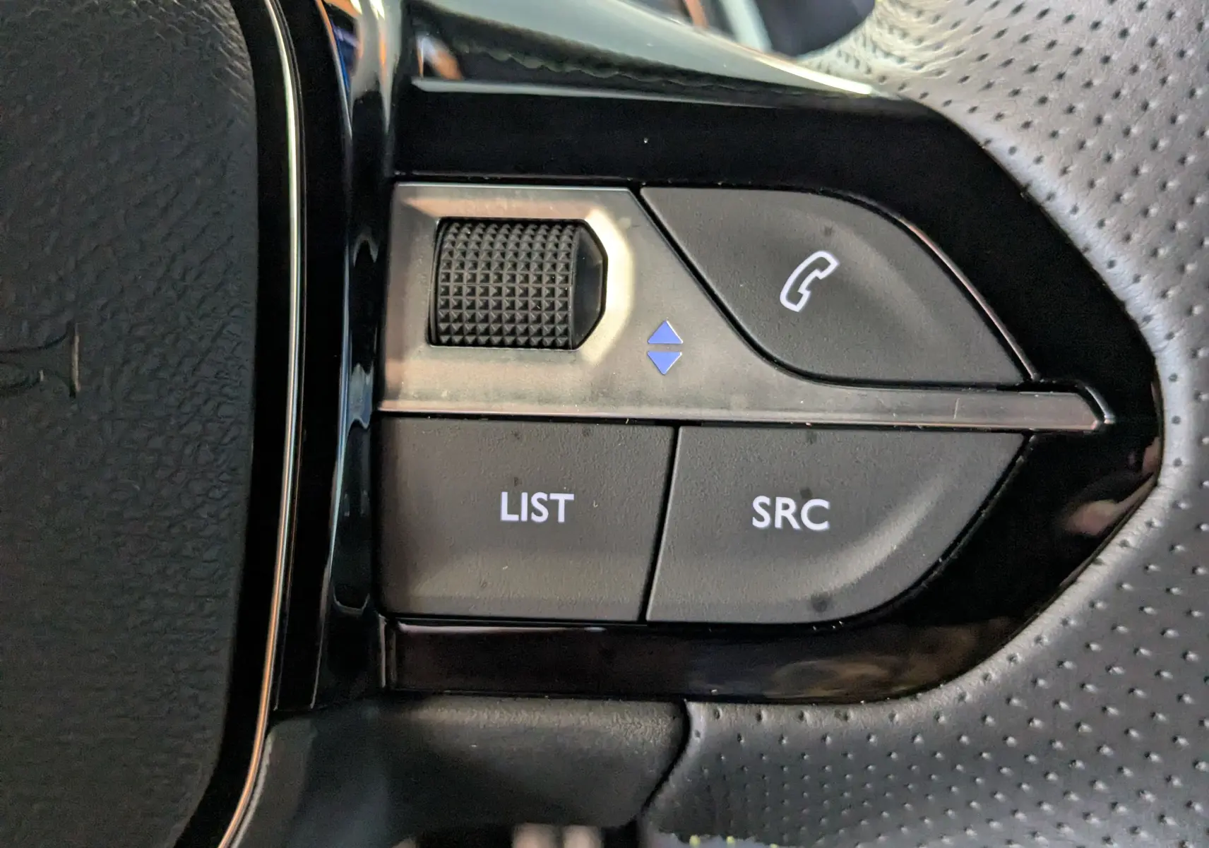 Gros plan sur les commandes du volant perforé de la Peugeot 208 Hybrid 145ch GT, boutons LIST, SRC et téléphone.