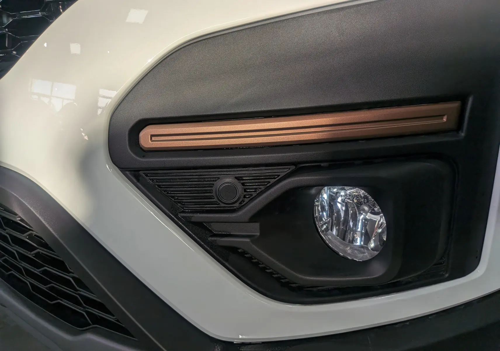 Gros plan sur le feu antibrouillard avant droit du Dacia Sandero Stepway blanc glacier avec insert décoratif cuivre.