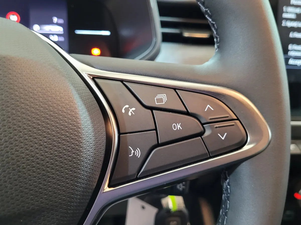 Gros plan sur les commandes multifonctions à droite du volant cuir de la Renault Clio bleu Evolution 2025.
