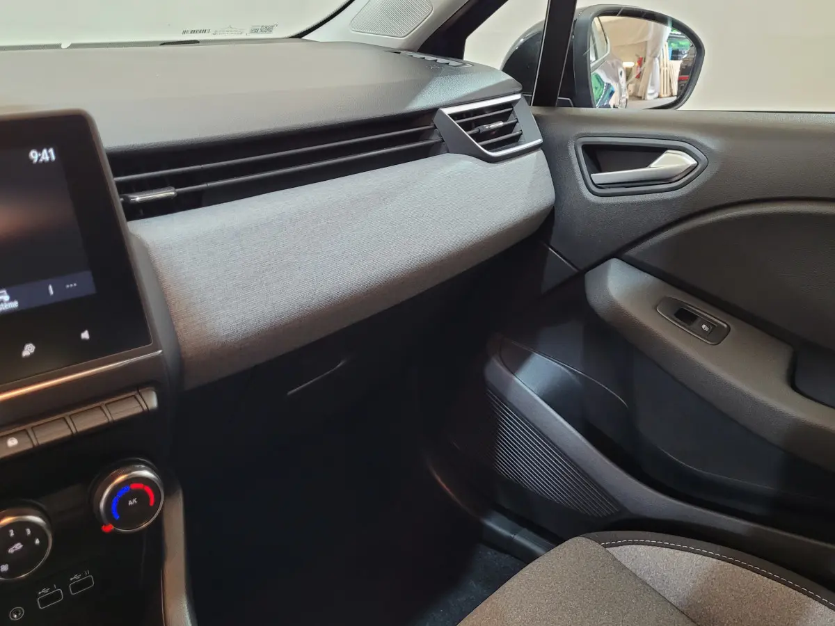 Intérieur côté passager de la Renault Clio bleu 2025 montrant tableau de bord gris clair et portière noire.