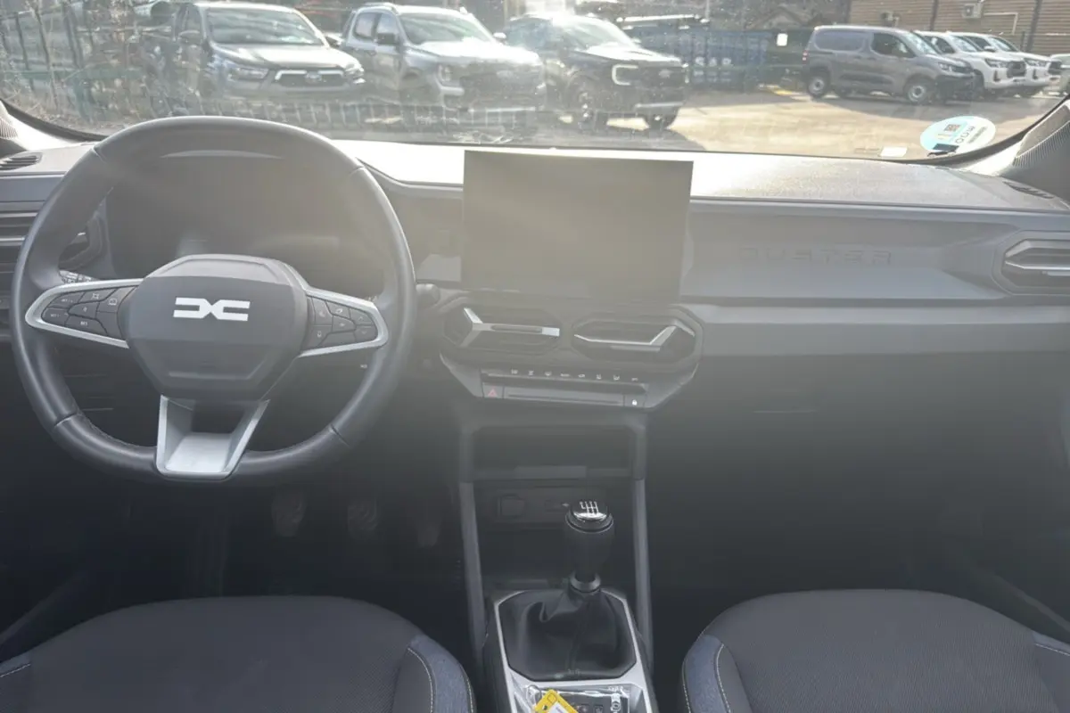 Vue intérieure frontale du tableau de bord du Dacia Duster 2025 avec volant cuir, écran tactile et levier de vitesses manuel.