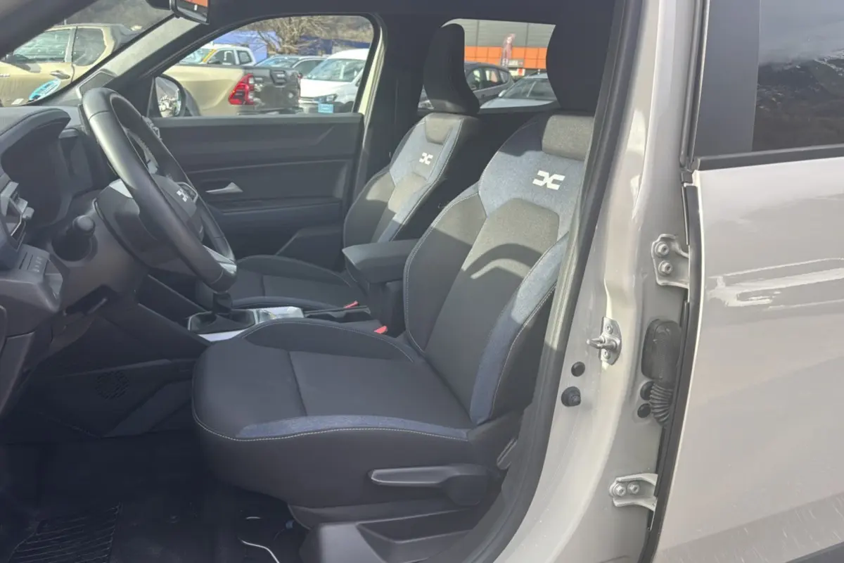 Vue intérieure côté conducteur du Dacia Duster 2025 Sandstone, sièges tissu avec logo distinctif et volant cuir soft feel.