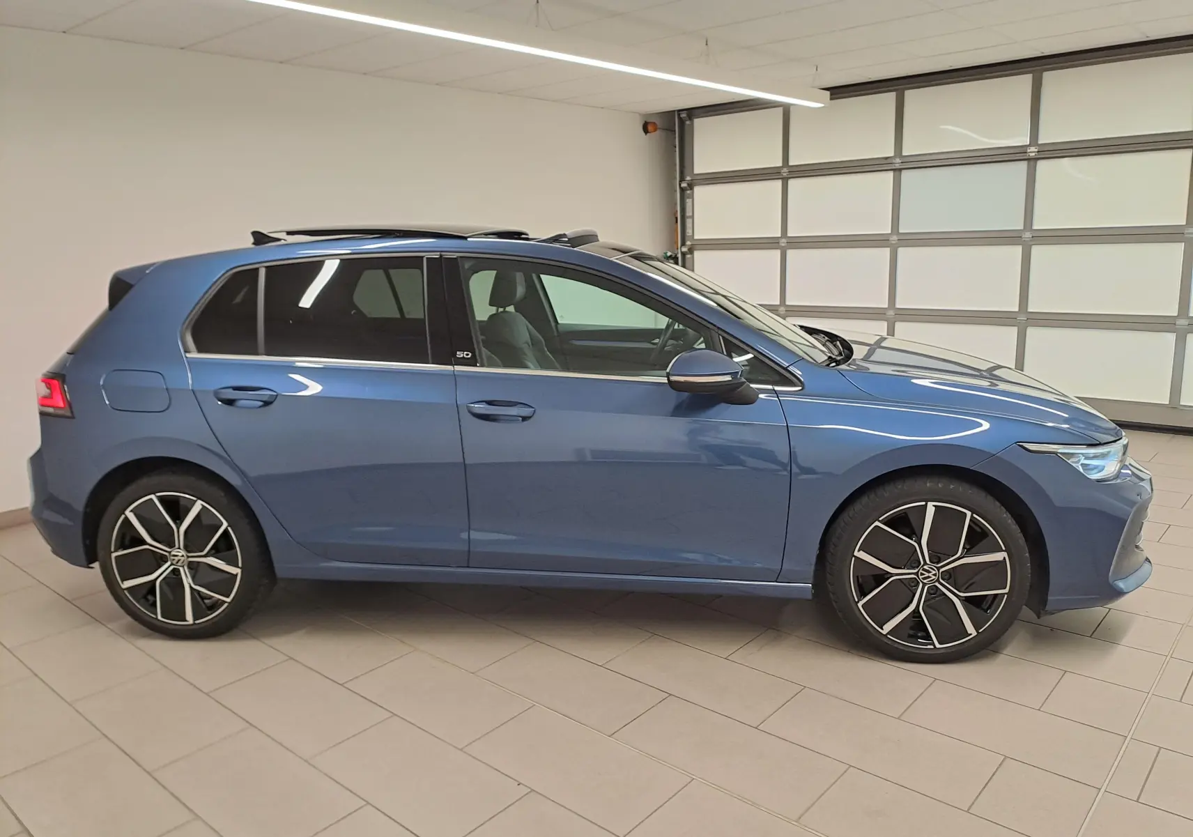 Volkswagen Golf 1.5 eTSI 2024 en bleu Anémone vue de profil côté gauche avec toit ouvrant panoramique et jantes alliage.