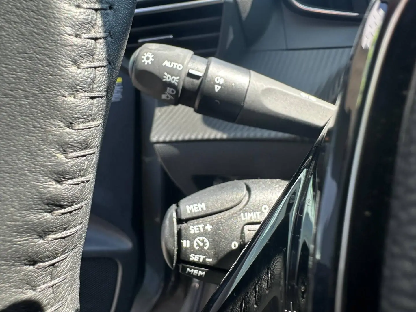 Gros plan sur les commandes au volant noir de la Peugeot 208 1.2 100ch Allure, avec détails des boutons de régulateur et phares.