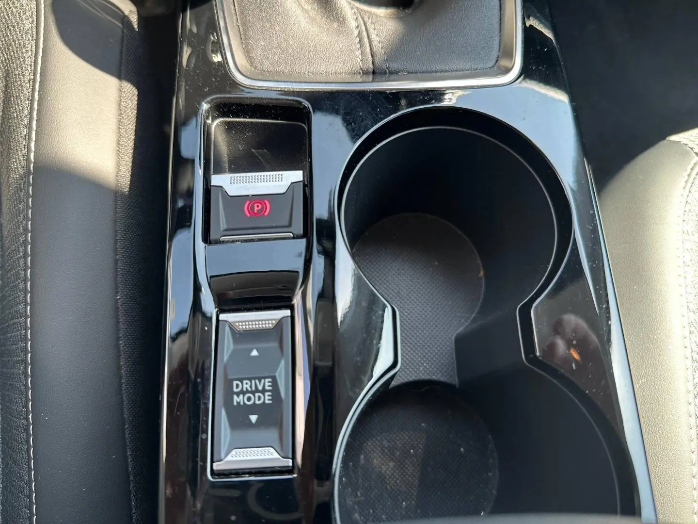 Gros plan sur la console centrale noire brillante de la Peugeot 208 2025, avec boutons frein électrique et mode de conduite.