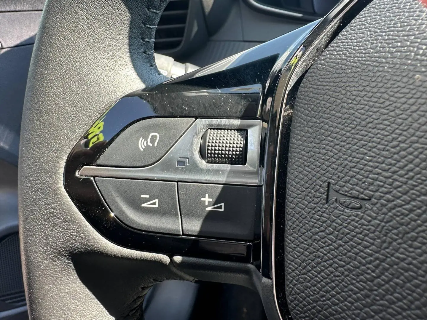 Gros plan sur les commandes noires du volant de la Peugeot 208 2025, avec boutons de volume et fonction mains-libres.