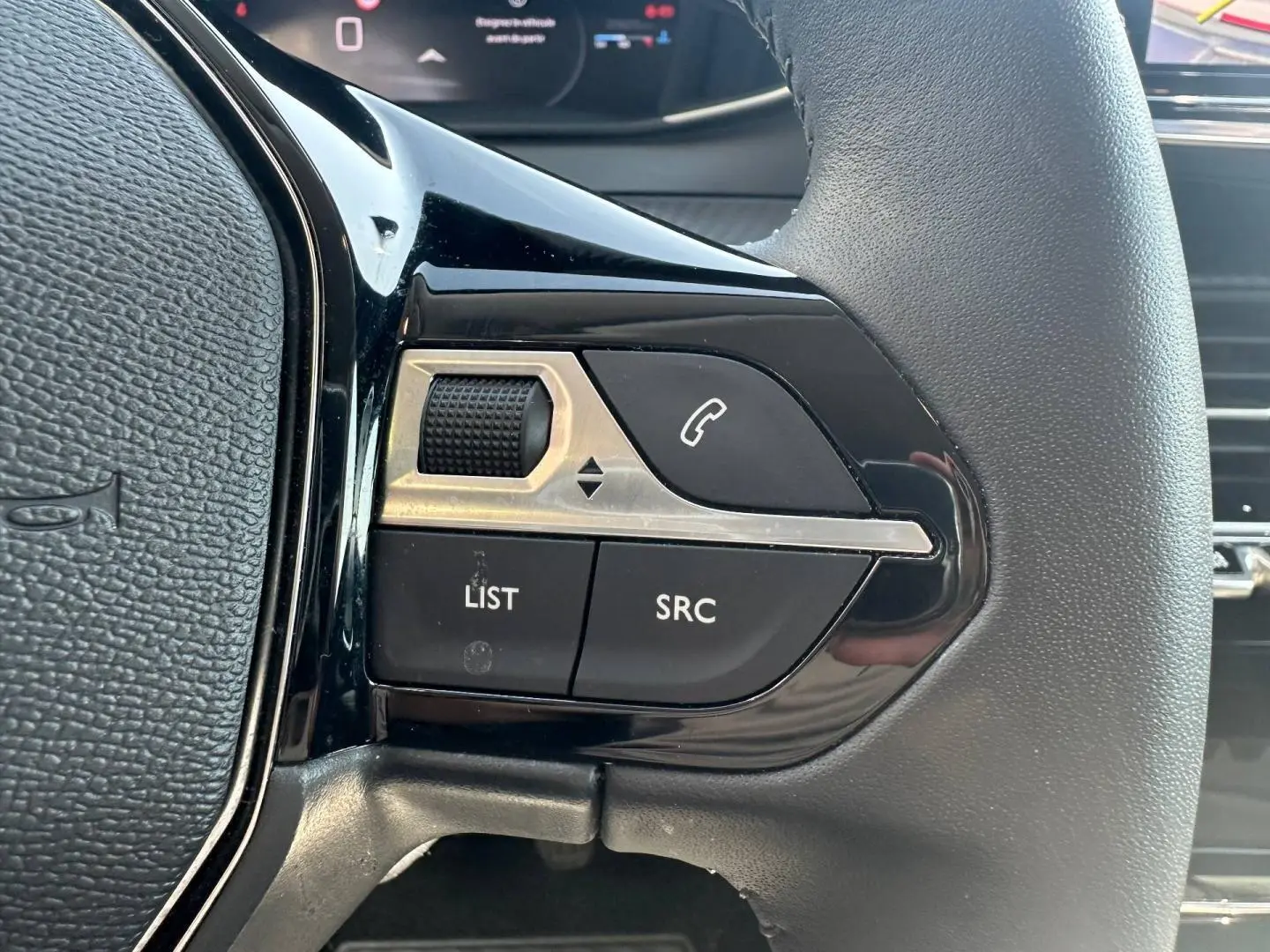 Gros plan sur les commandes gauche du volant noir de la Peugeot 208 Gris Selenium avec boutons audio et téléphone.