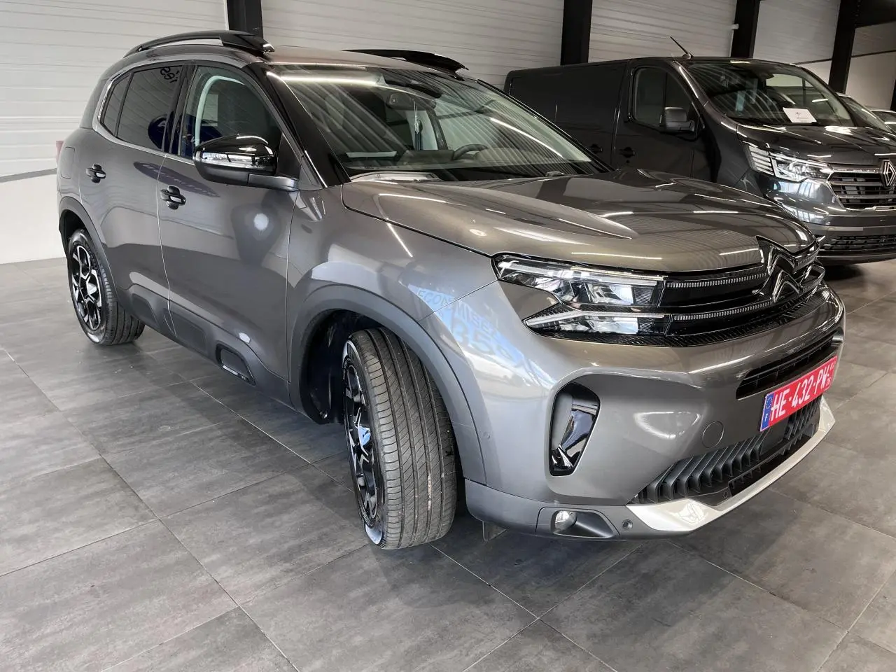 Citroën C5 Aircross gris platinium en 3/4 avant droit, avec jantes alliage bi-ton et barres de toit noires.