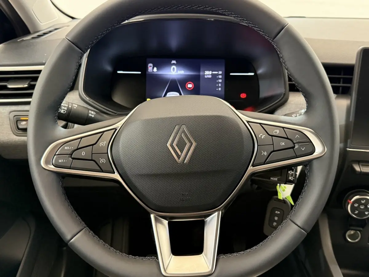 Vue rapprochée du volant cuir noir avec commandes multifonctions et logo Renault au centre du tableau de bord d’une Clio 2025.