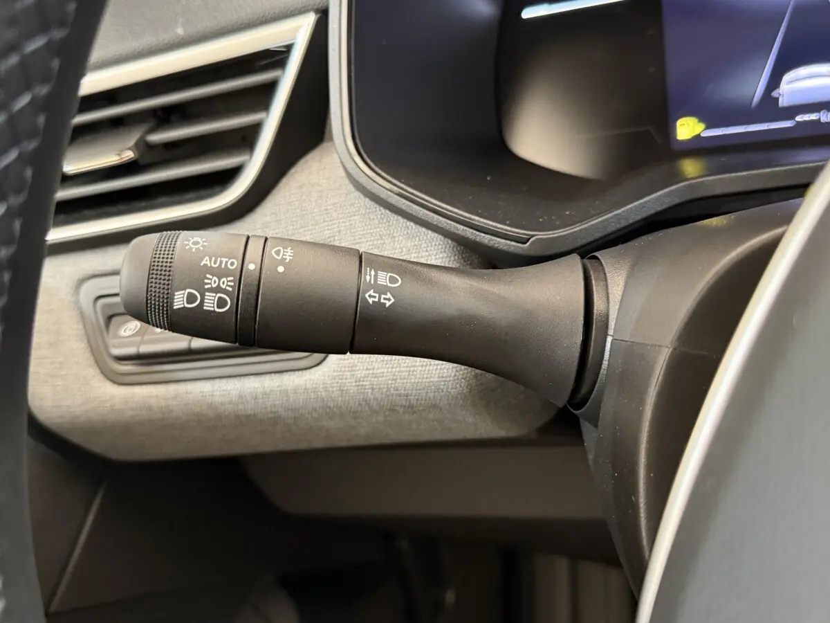 Gros plan sur la commande des phares et clignotants dans l'habitacle gris clair de la Renault Clio noire 2025.